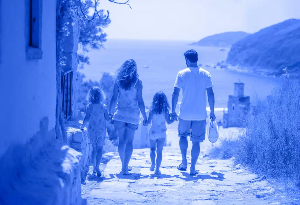 Four people walking down a stone path toward the sea in a coastal town
