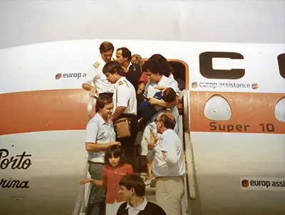 Group of passengers, including airline crew, standing on aircraft stairs and exiting a plane marked with Europ Assistance branding and the text 'Super 10'