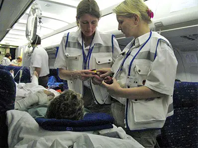 Two medical professionals in uniform attending to a patient lying on a seat inside an airplane cabin, with medical equipment visible